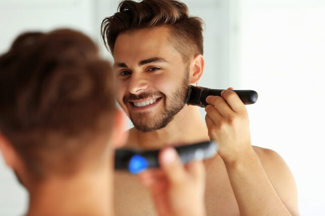 鏡に向かってにこやかな顔でシェーバーで髭剃りしている男性